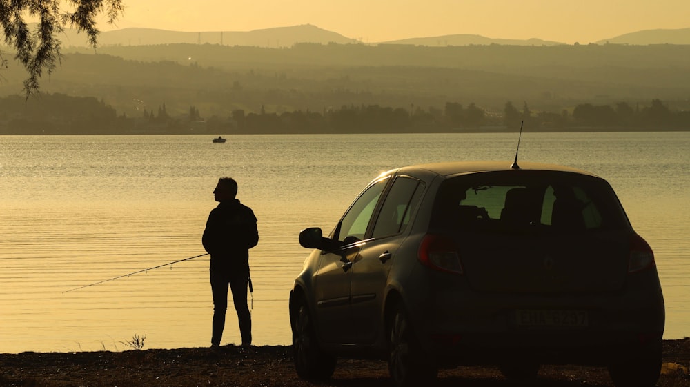 a man standing next to a car near a body of water