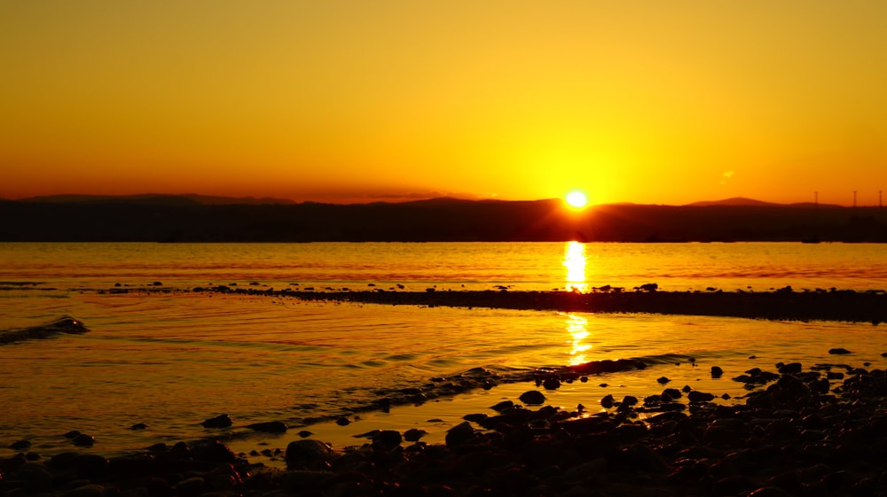 a sunset over a body of water with rocks in the foreground