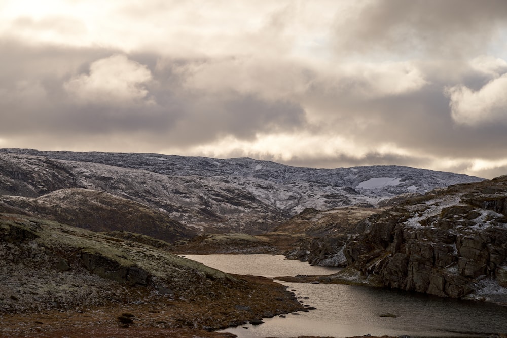 a lake surrounded by mountains under a cloudy sky