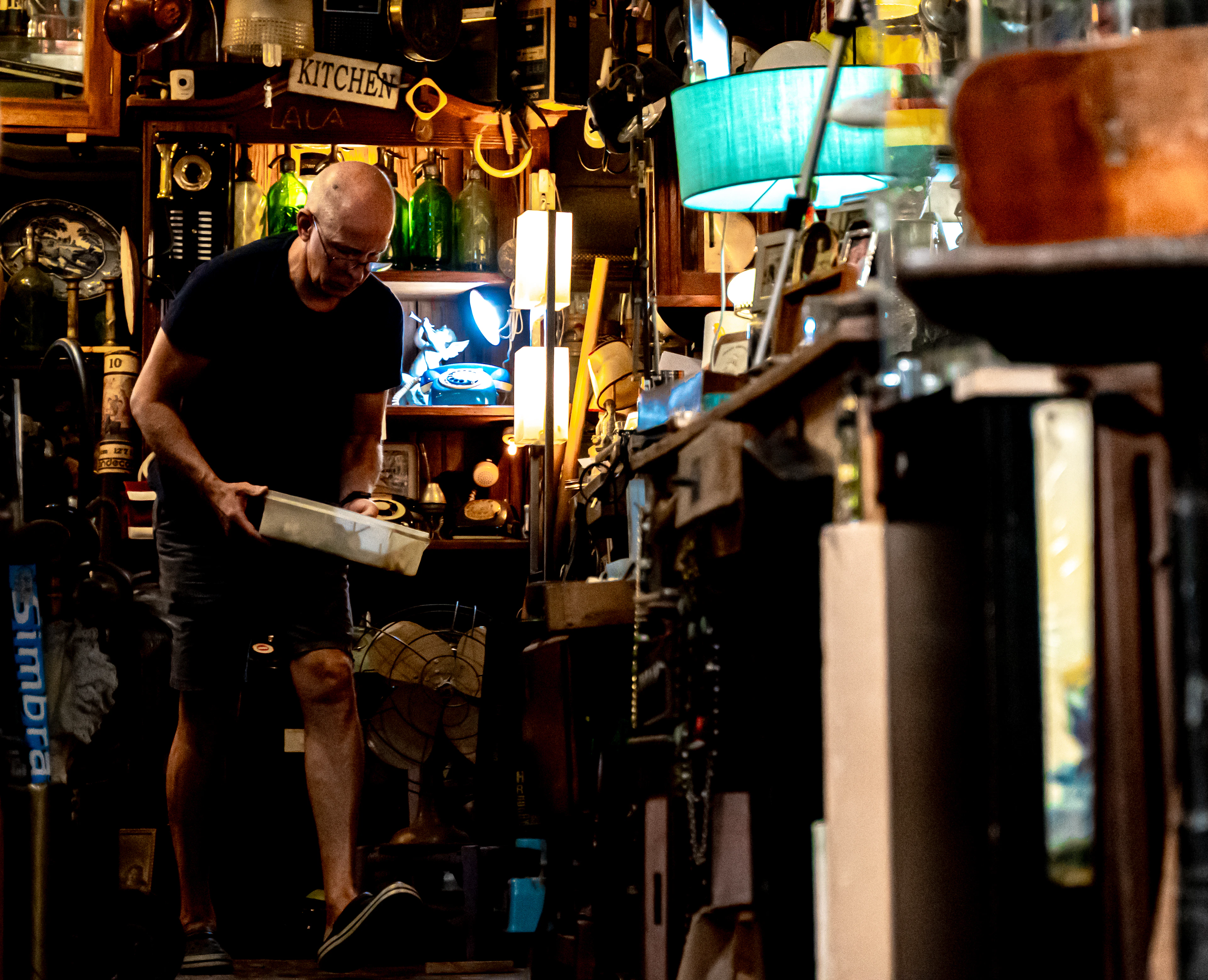 A man sorts through crowded shelves of vintage lamps and bric-a-brac in an antiques shop.
