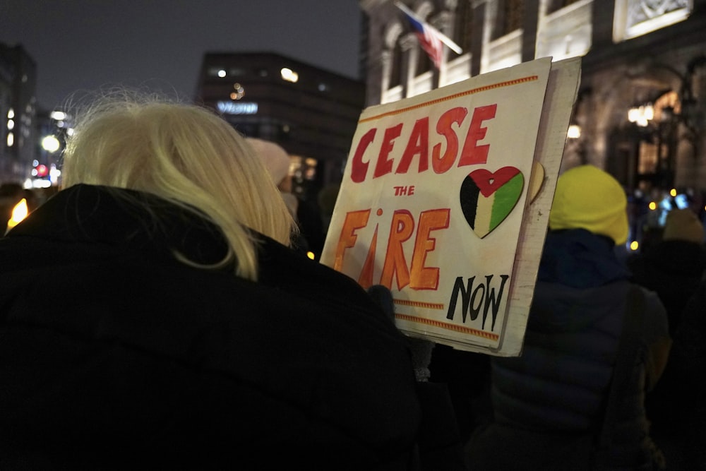 Eine Frau hält ein Schild mit der Aufschrift "Bitte jetzt das Feuer"