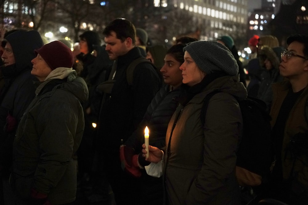 un gruppo di persone in piedi l'una intorno all'altra con in mano una candela