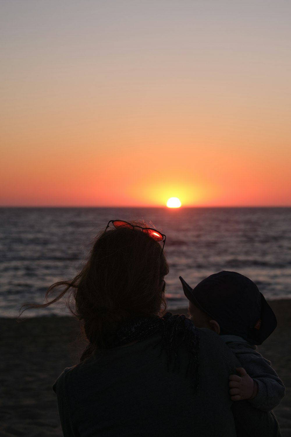 a woman holding a child on the beach at sunset