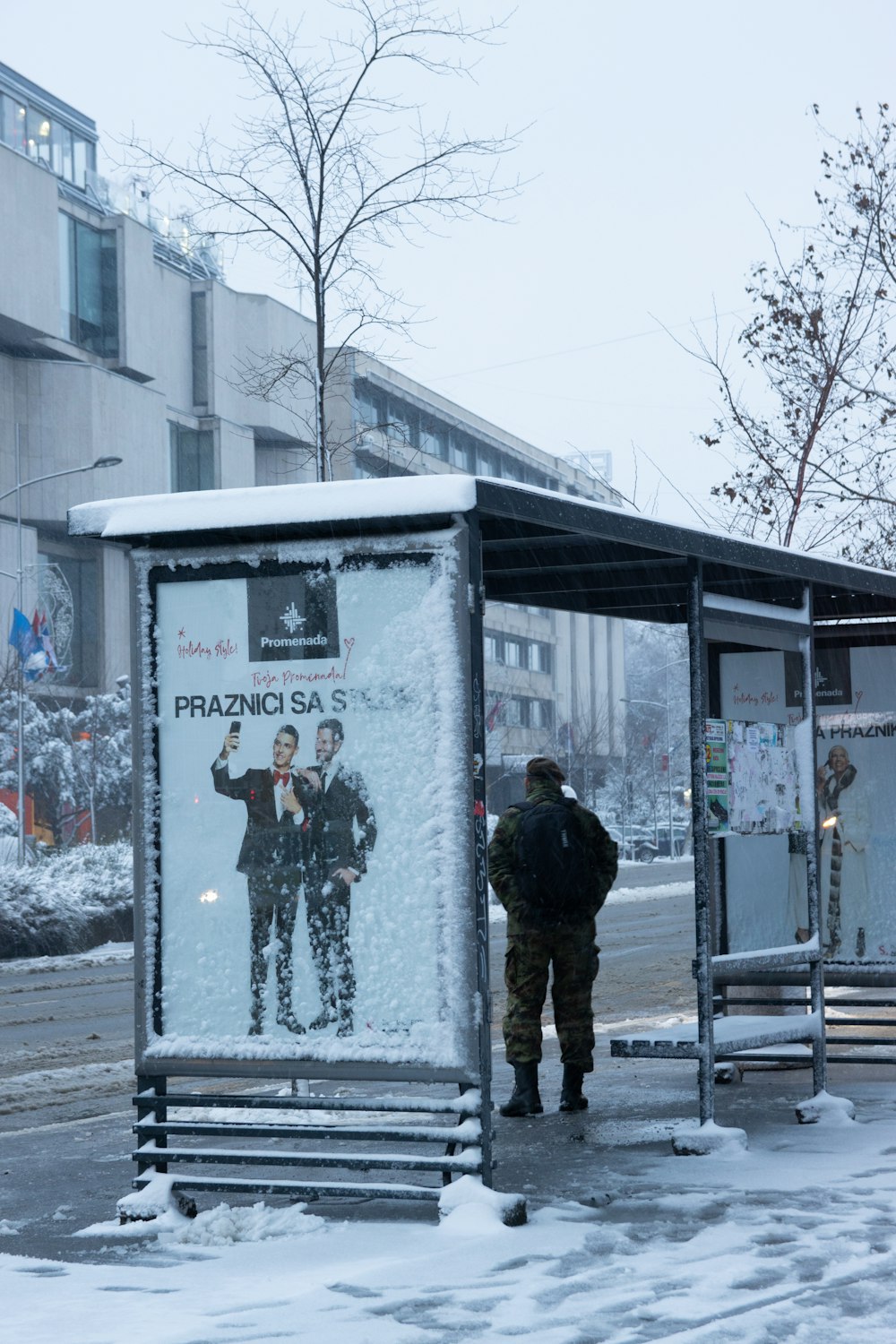 a man standing next to a bus stop covered in snow