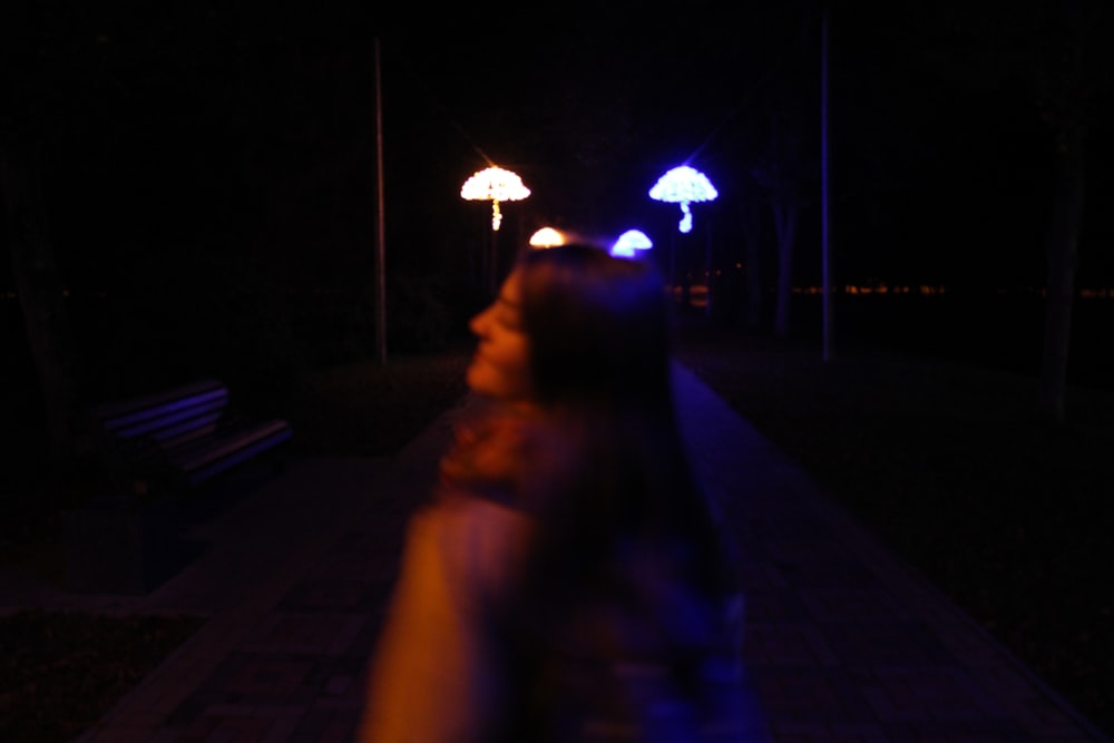 a woman walking down a sidewalk at night