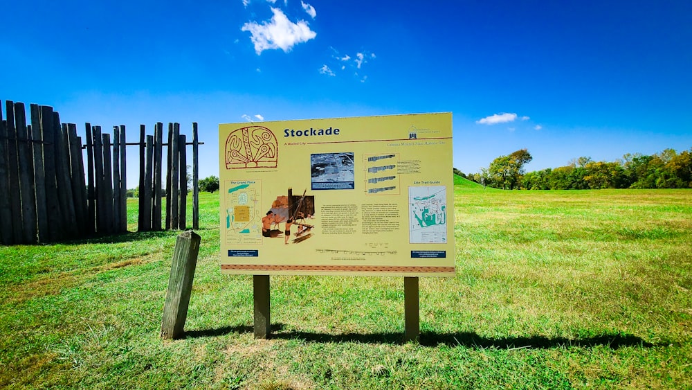 a sign in a grassy field with a fence in the background