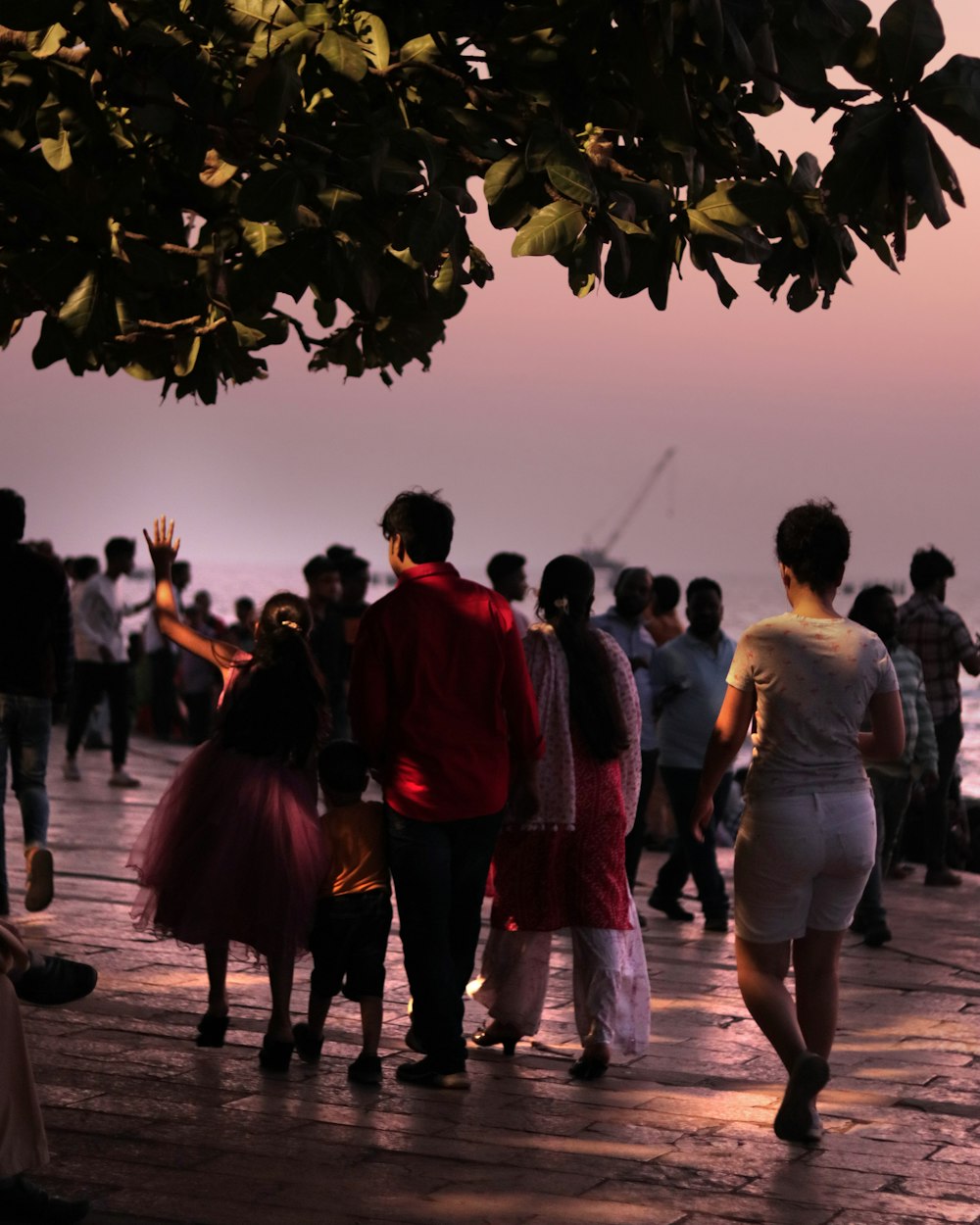 a group of people walking down a sidewalk next to the ocean