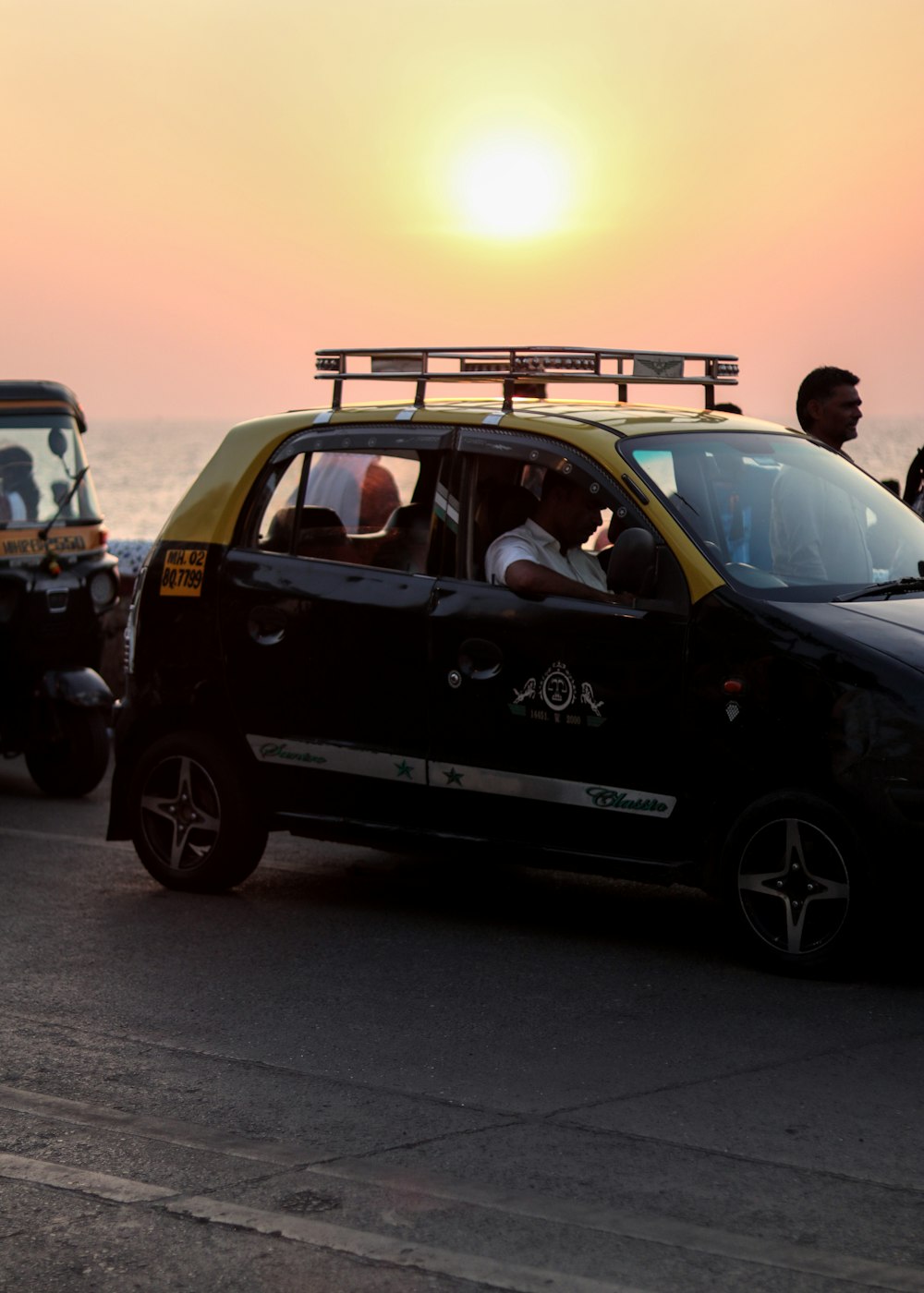 a small black car driving down a street next to the ocean