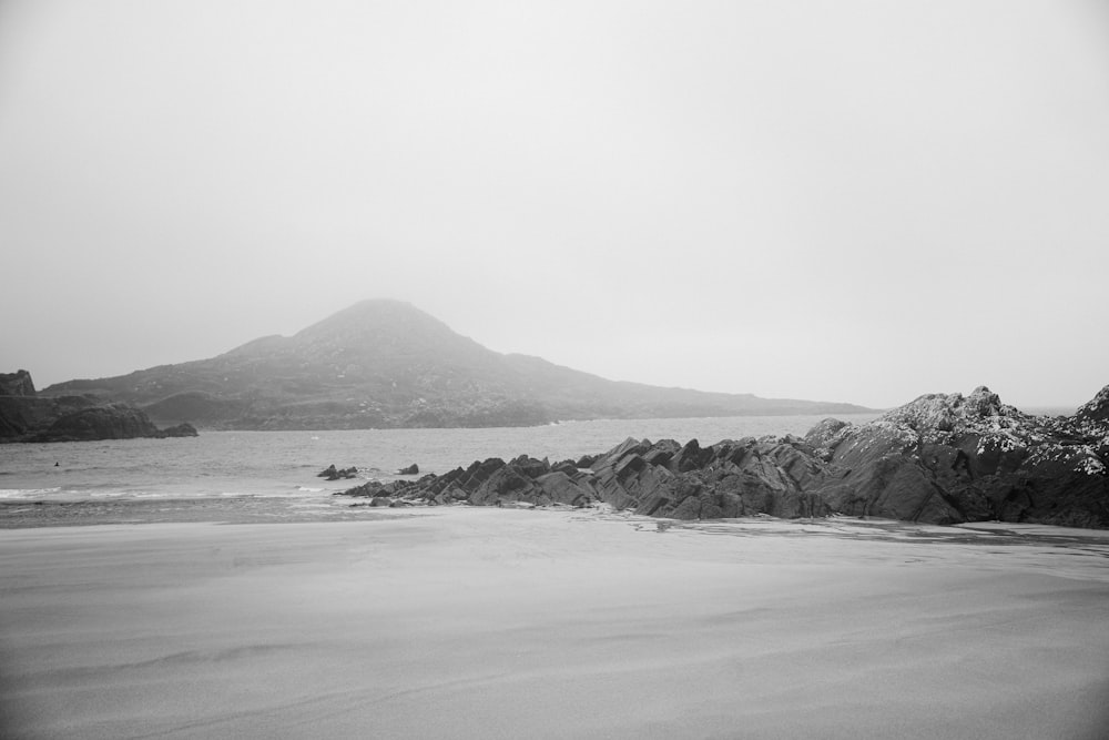 a black and white photo of a beach with a mountain in the background