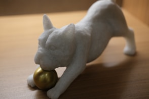 a white cat figurine with a golden ball on a table