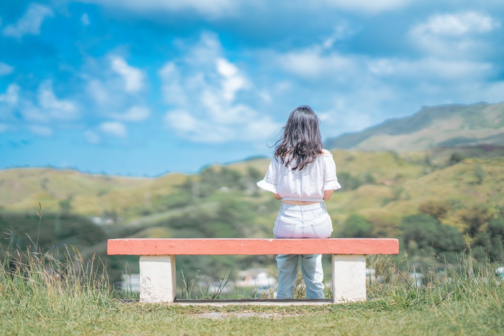 a woman sitting on top of a bench in a field