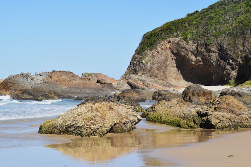 a beach with rocks and water and a hill in the background