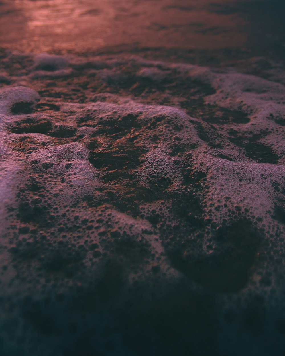 a close up of sand and water with a sunset in the background
