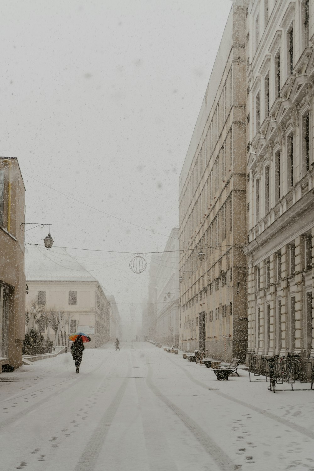 eine Person, die mit einem Regenschirm eine verschneite Straße entlanggeht