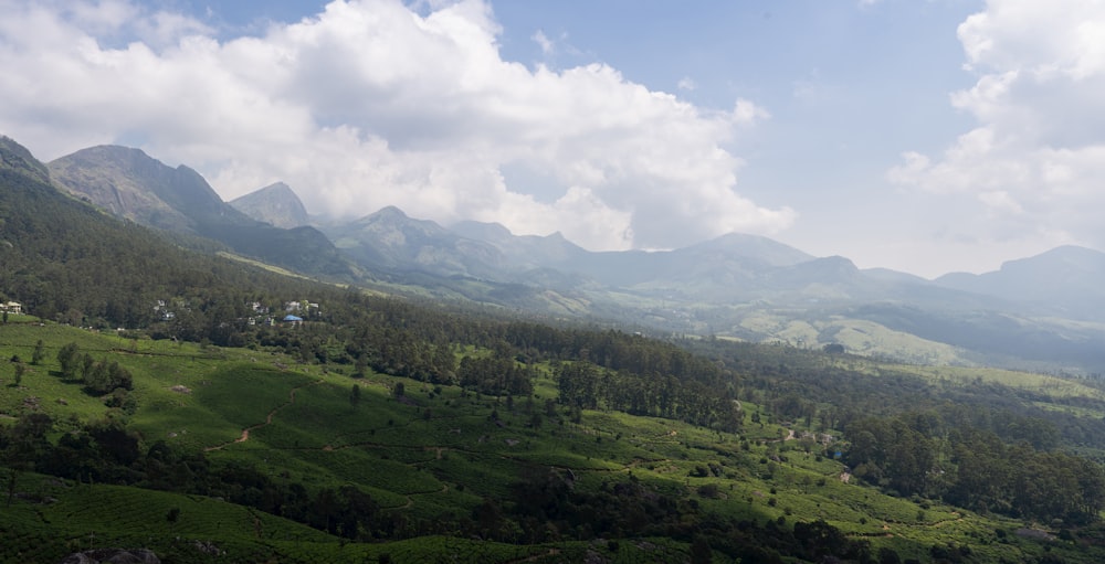 a lush green valley surrounded by mountains under a cloudy blue sky