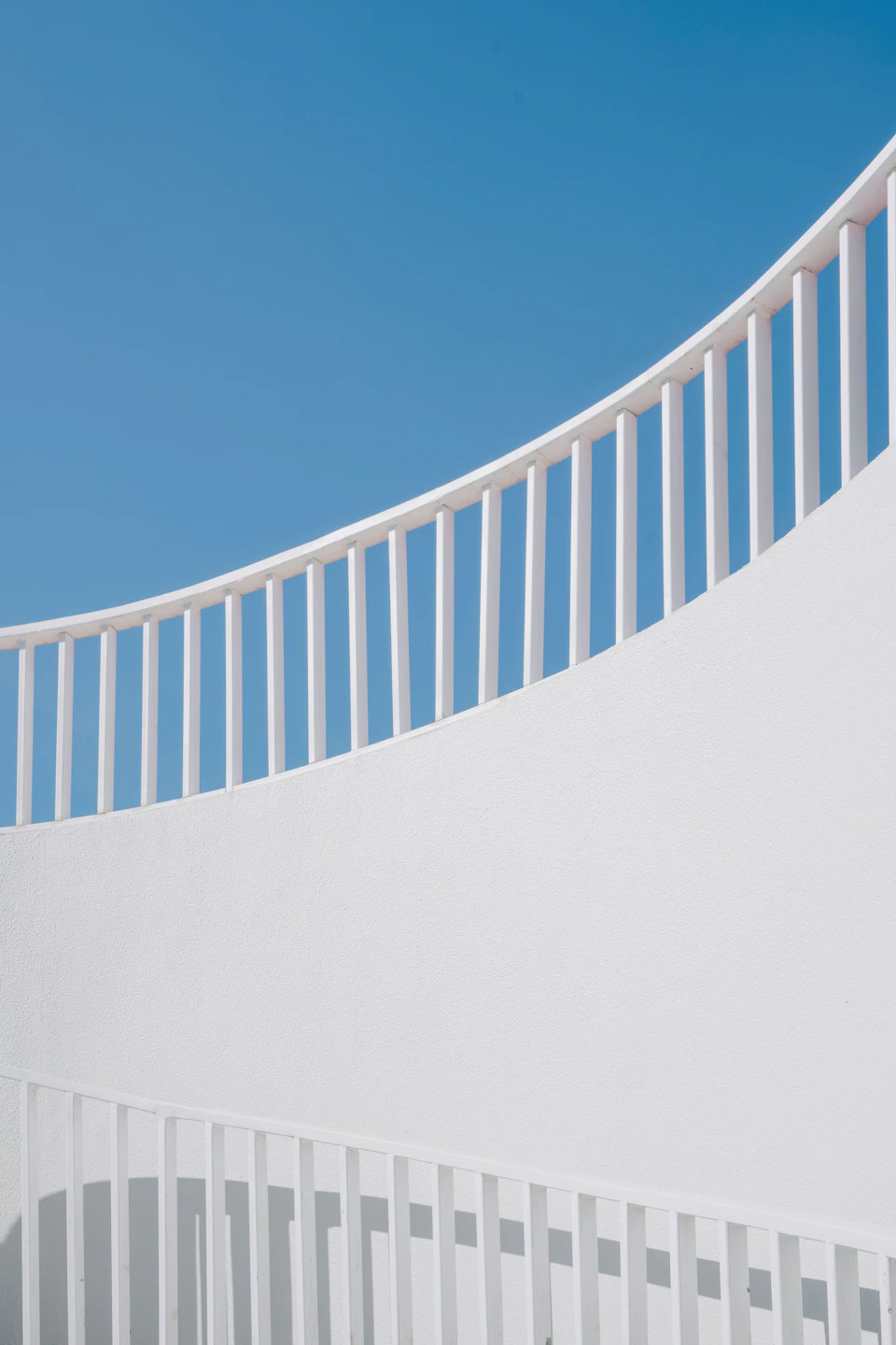 White railing with vertical bars set against clear blue sky, extending across the frame horizontally