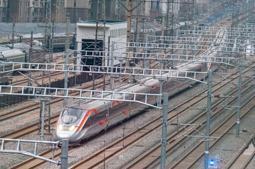 a silver train traveling down train tracks next to tall buildings