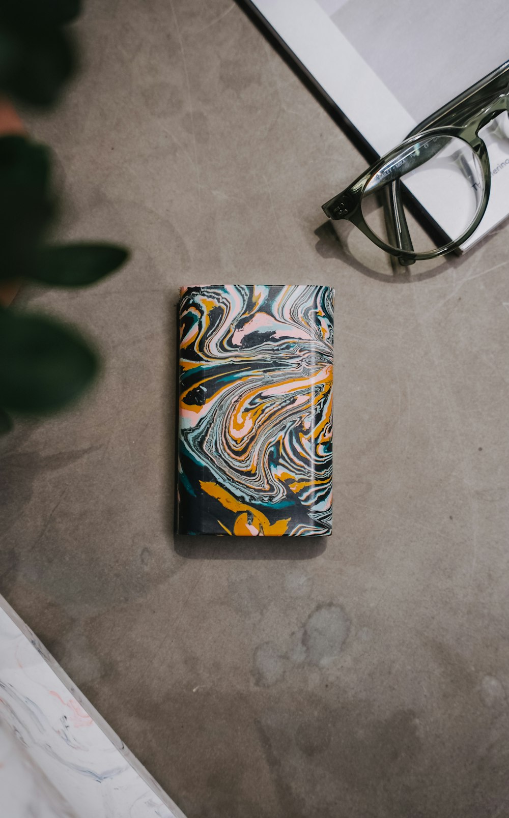 um caderno com uma capa marmorizada sentado em uma mesa ao lado de um par de