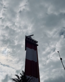a tall red and white tower under a cloudy sky