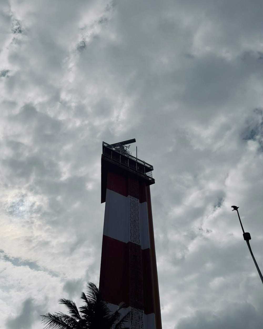 a tall red and white tower under a cloudy sky