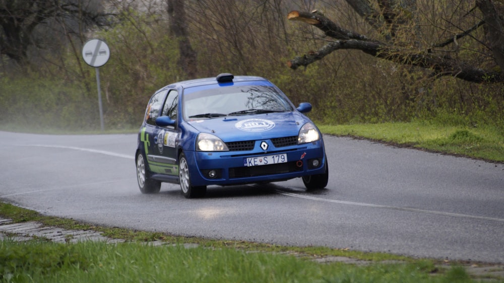 a blue car driving down a road next to a forest