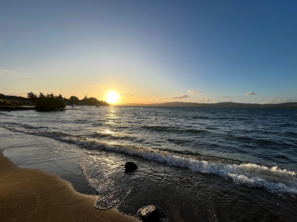 the sun is setting over the water at the beach