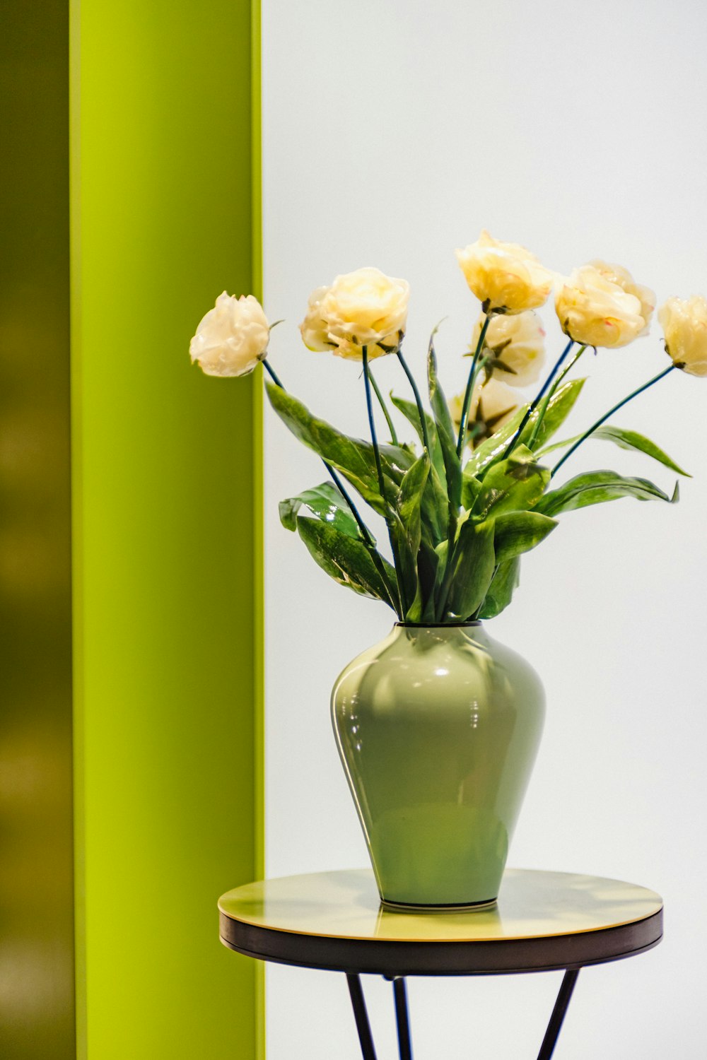 a green vase with yellow flowers on a small table