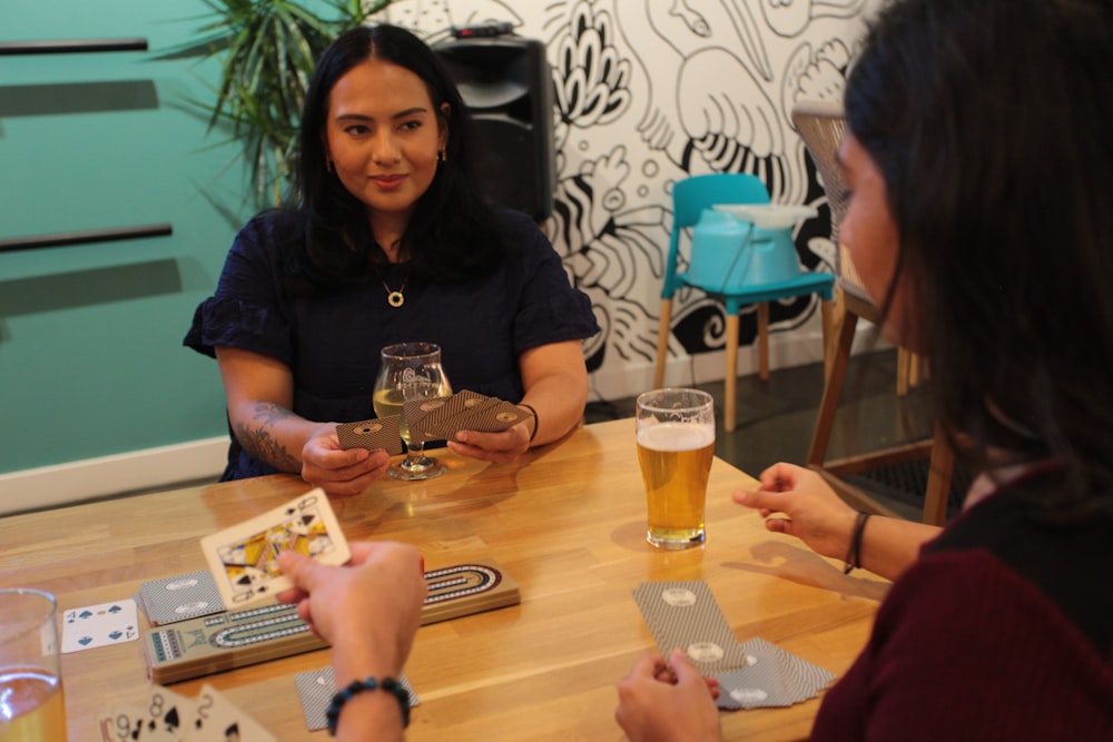 two women sitting at a table with cards and a glass of beer