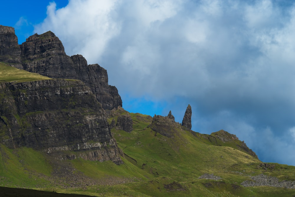 a green mountain with a few clouds in the sky