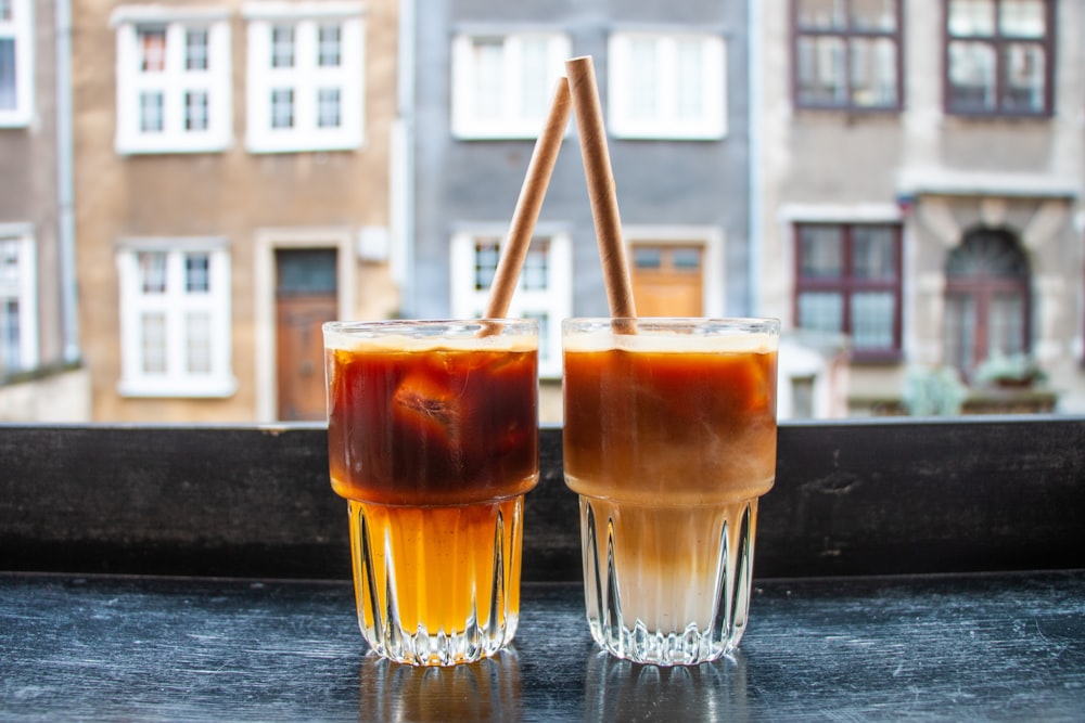 two glasses of iced coffee sit on a window sill