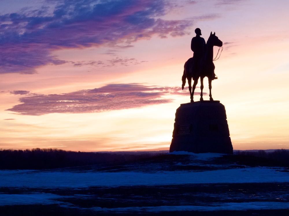 a statue of a man riding a horse at sunset