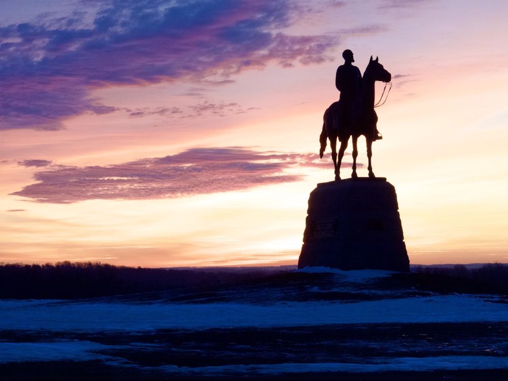 une statue d’un homme chevauchant un cheval au coucher du soleil