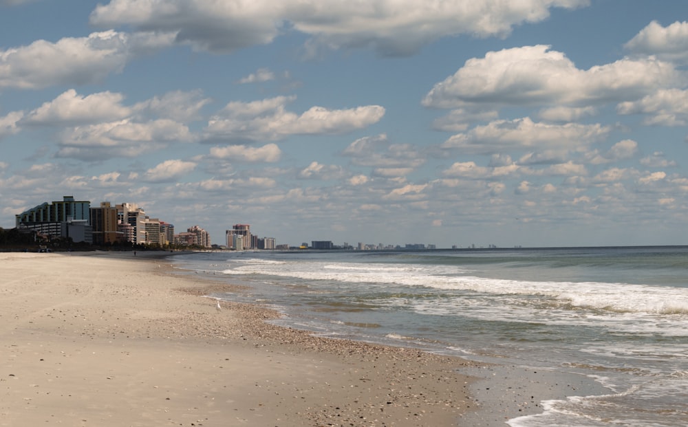 a sandy beach next to the ocean under a cloudy blue sky