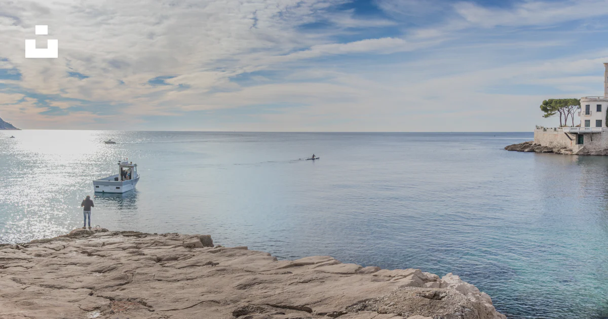 A Man Standing On The Edge Of A Cliff Overlooking A Body Of Water Photo a-man-standing-on-the-edge-of-a-cliff-overlooking-a-body-of-water-photo