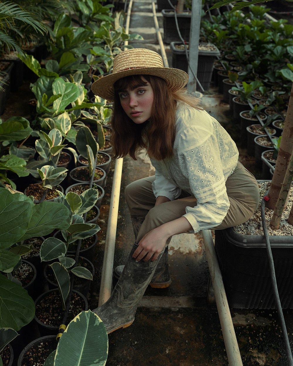 a woman in a straw hat is kneeling down in a greenhouse