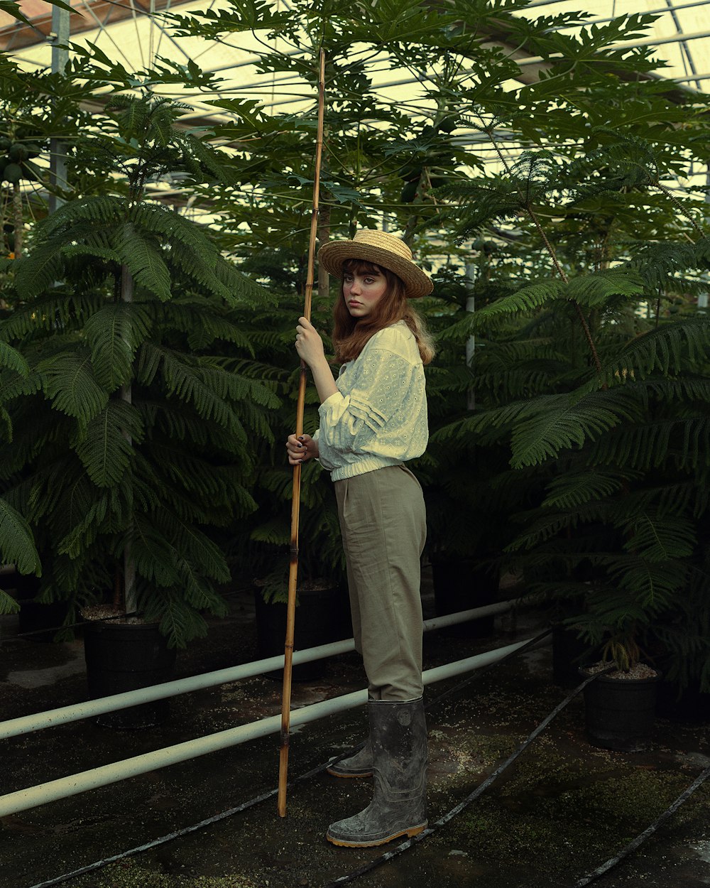 a woman standing in a greenhouse holding a stick