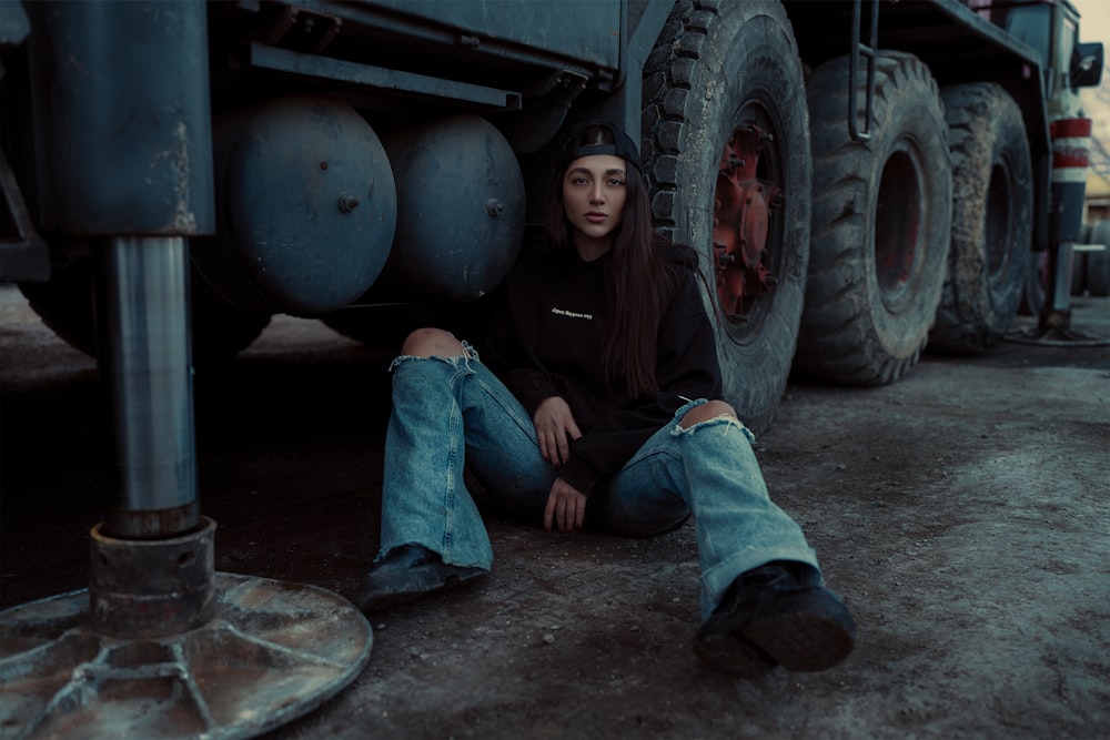 a woman sitting on the ground next to a large truck