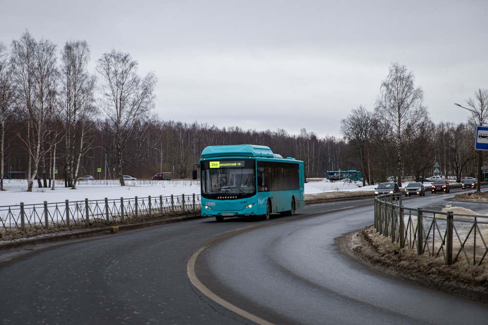 a blue bus driving down a snow covered road