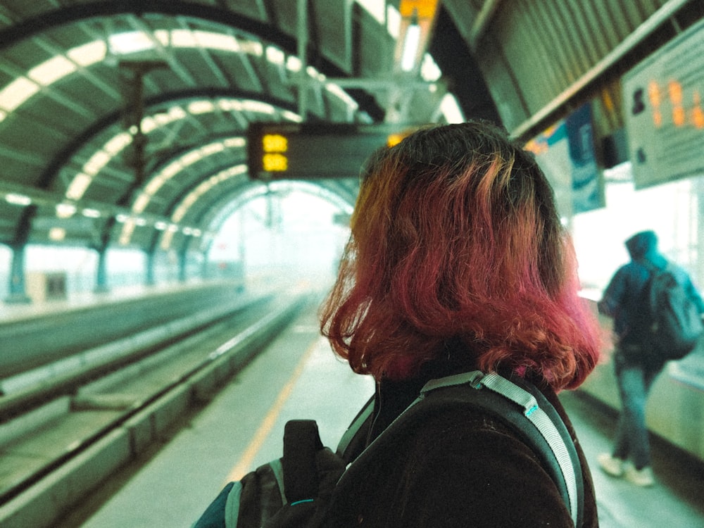 a woman with red hair is waiting for a train