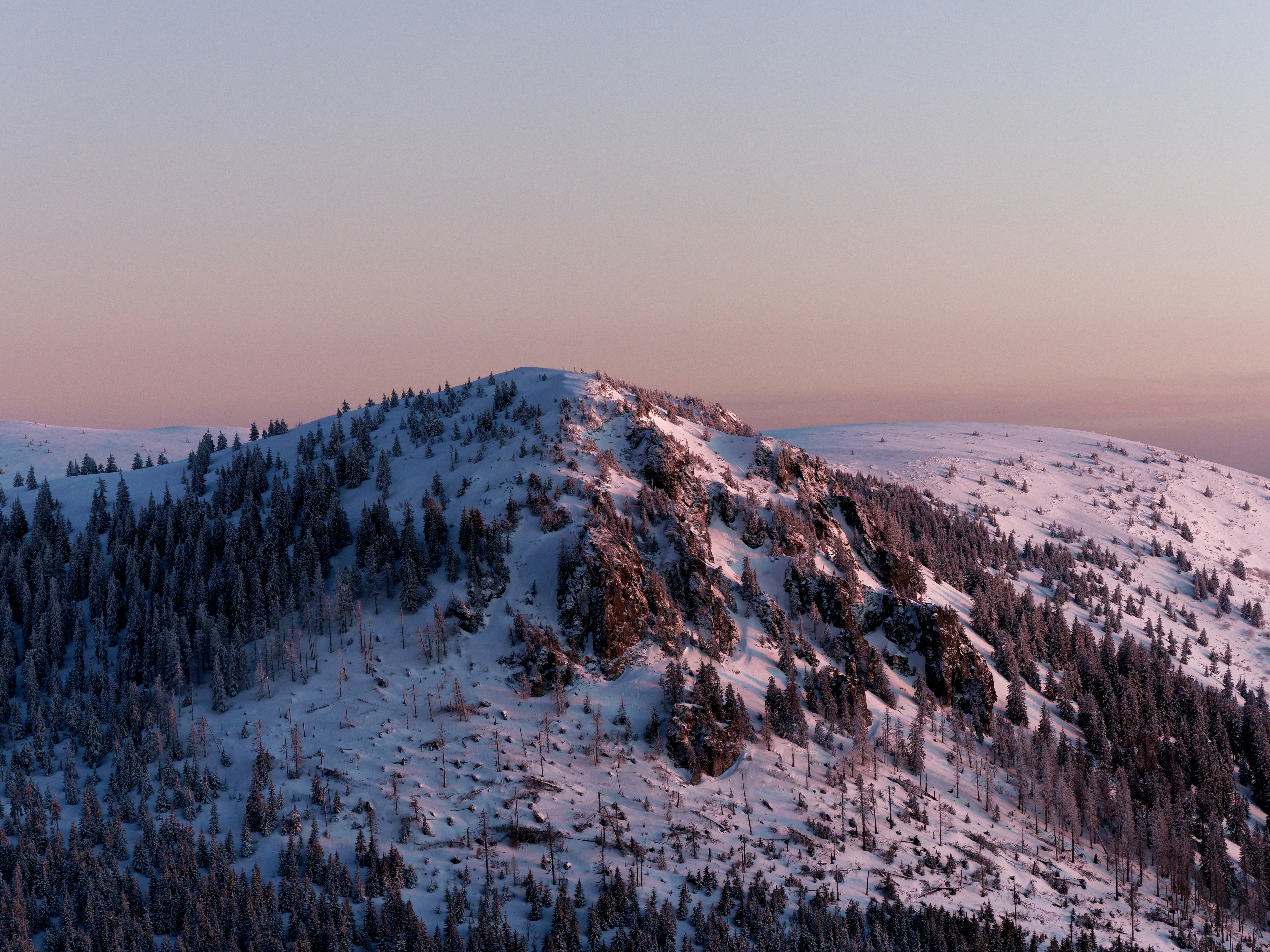 a mountain covered in snow and trees under a pink sky