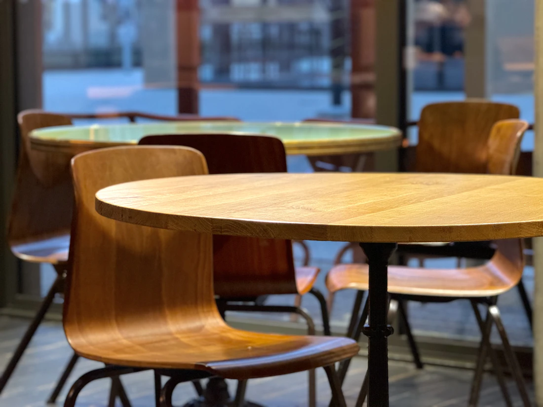 Runde Tischplatten aus Eiche mit geschwungenen Holzstühlen, Morgenlicht im Café