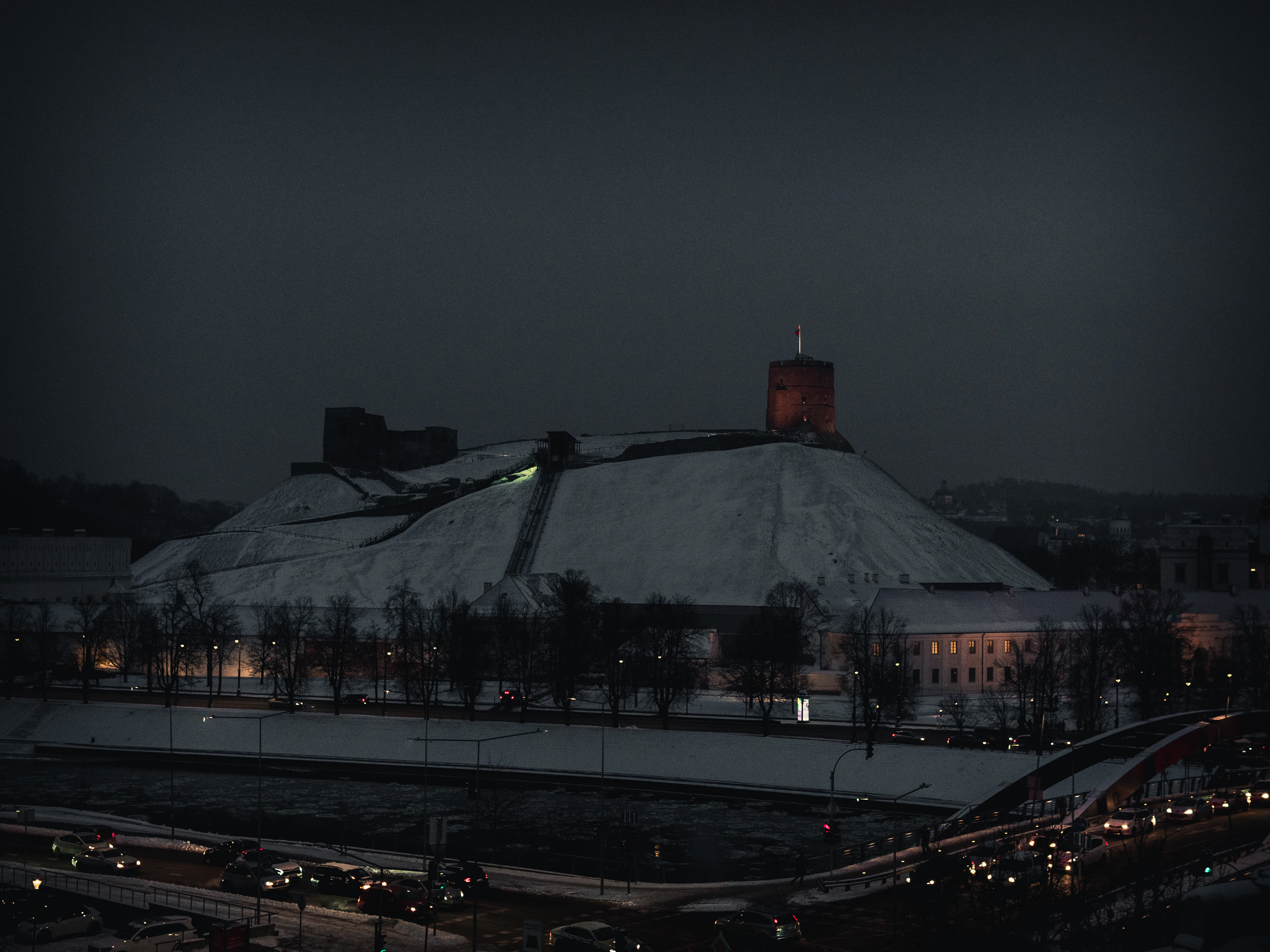 Winter dusk in Vilnius: snow-covered Gediminas Hill with its castle tower, car lights on the road below
