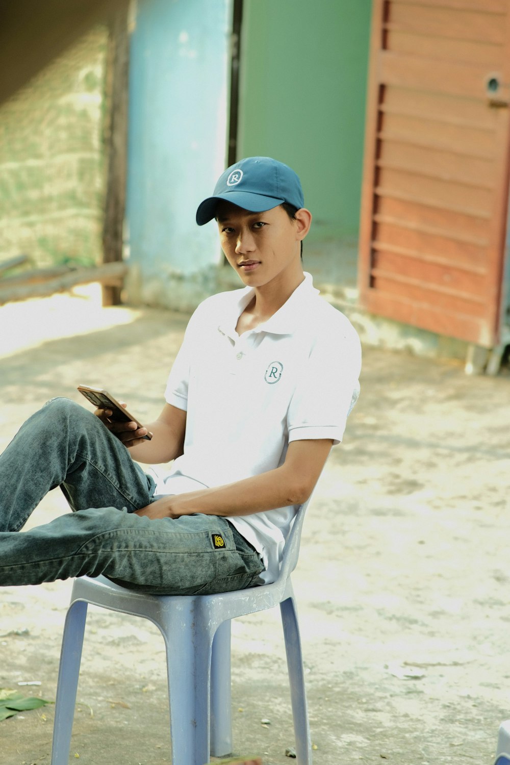 a young man sitting on a chair with a baseball cap on