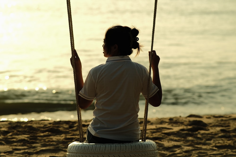 a woman sitting on a tire swing at the beach