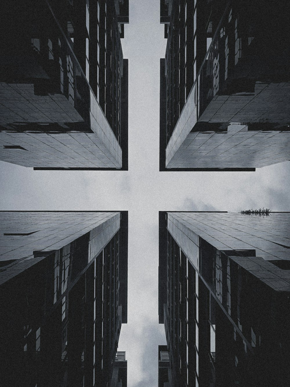 a black and white photo of a cross in the middle of tall buildings