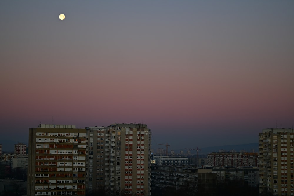 a full moon rising over a city with tall buildings