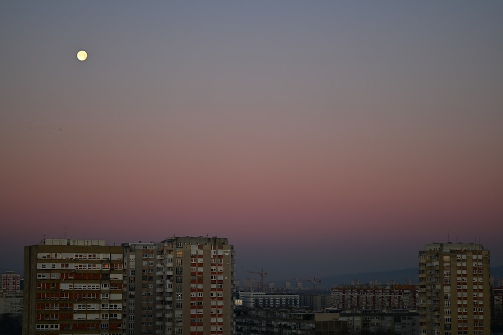 a full moon rising over a city with tall buildings