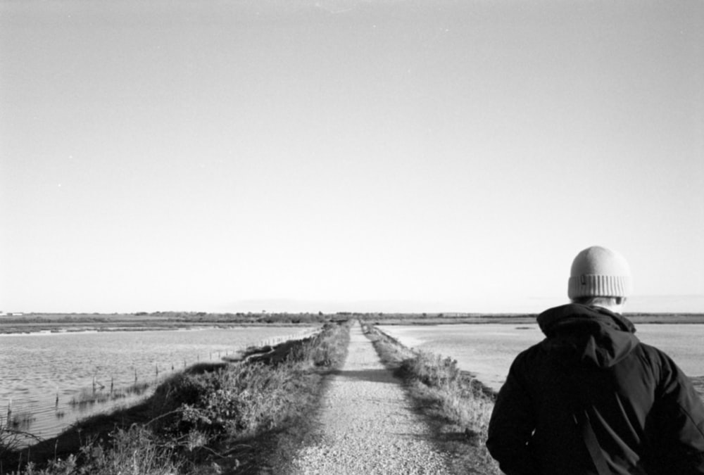 a person walking down a dirt road next to a field