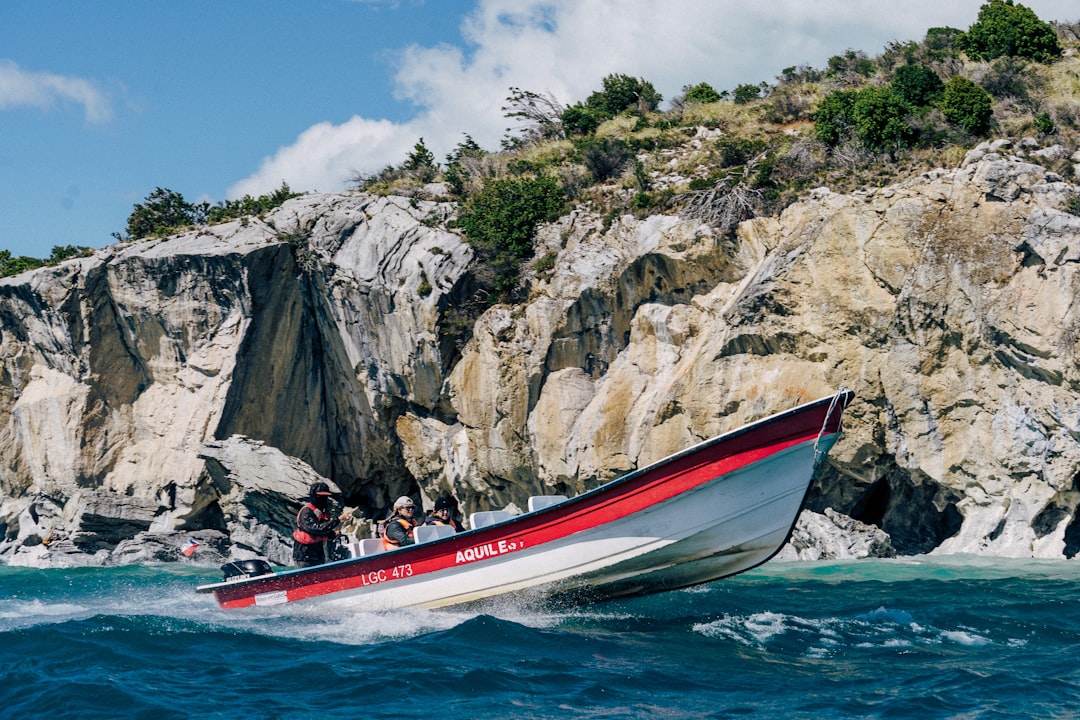 a red and white boat traveling past a rocky cliff,