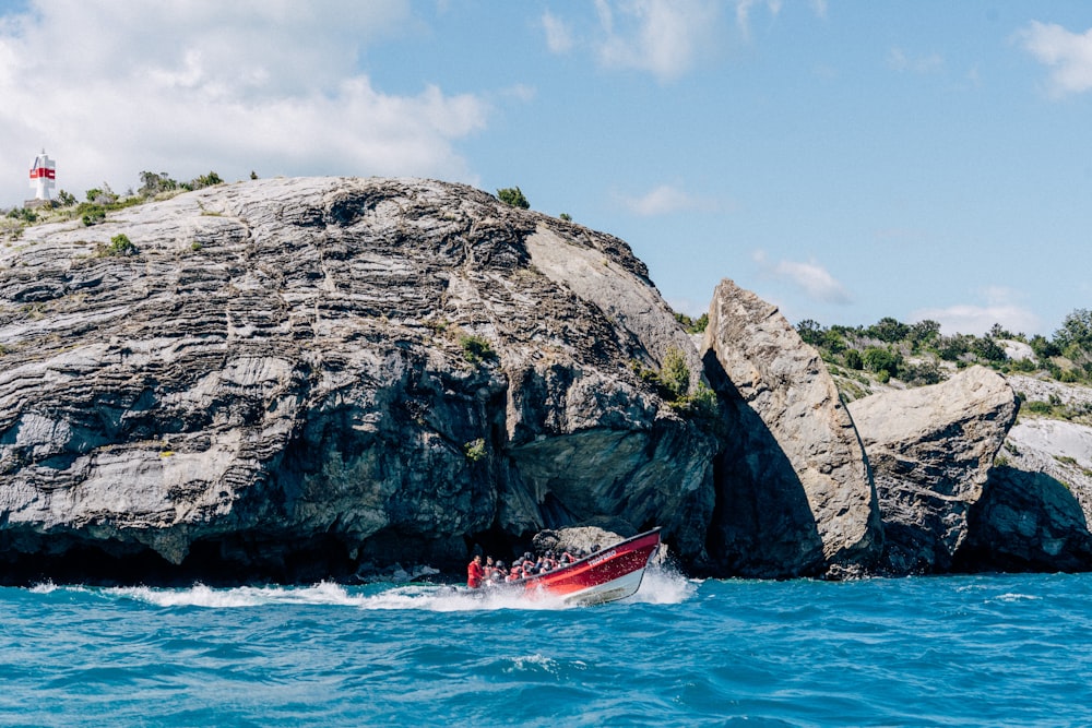 a red boat in a body of water near a large rock